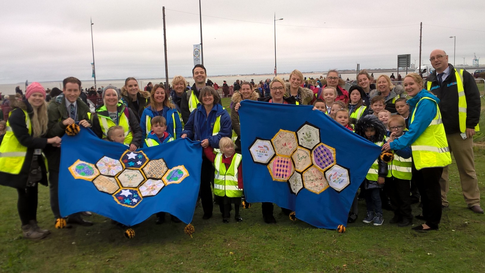 school children in wirral holding up their giant artworks featuring their dreams flanked by two teachers in high vis