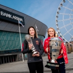 two ladies stood outside mands bank arena and the liverpool wheel holding netball and rugby tropies