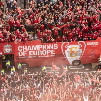 red LFC bus with players on top on road in liverpool surrounded by crowds