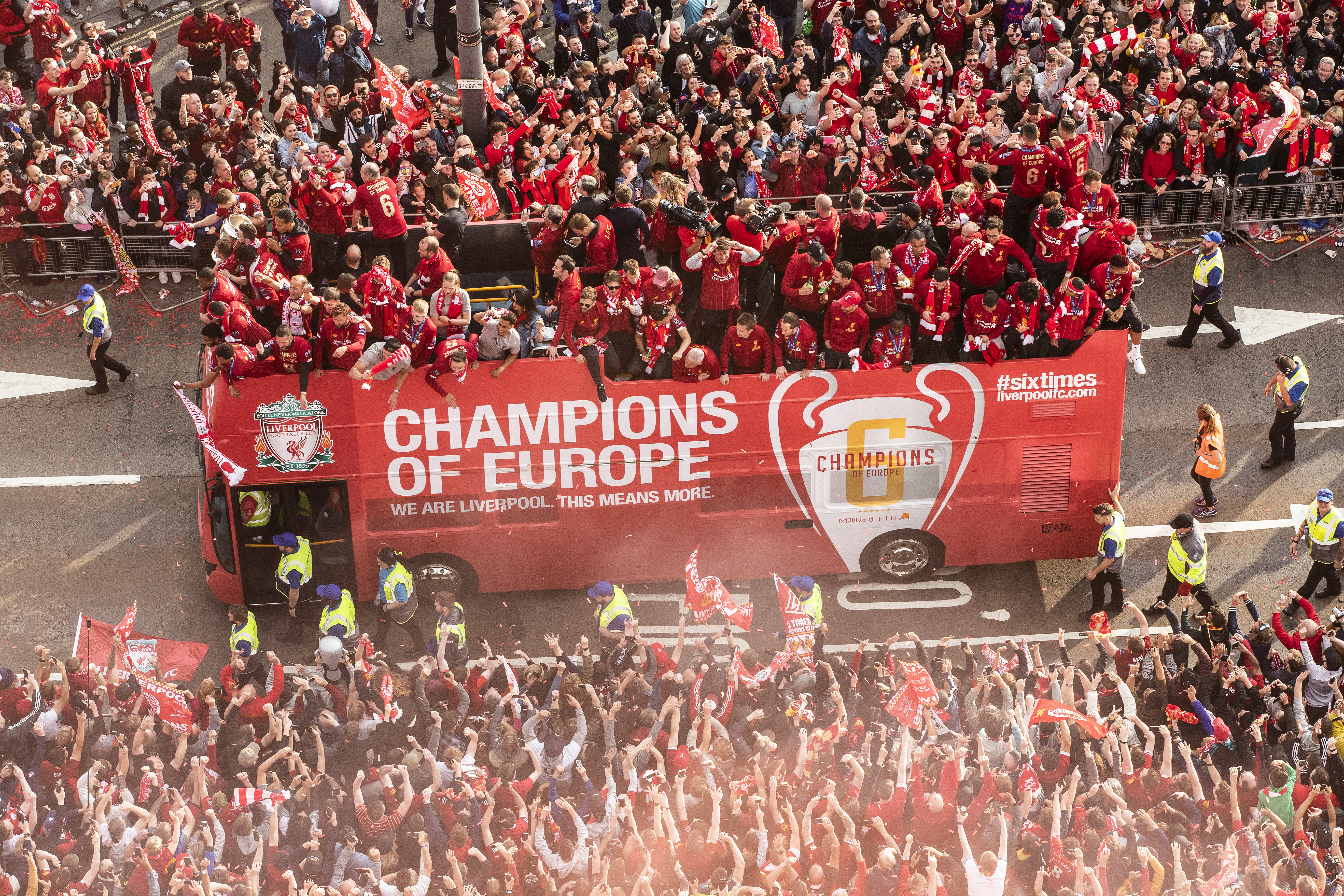 red LFC bus with players on top on road in liverpool surrounded by crowds