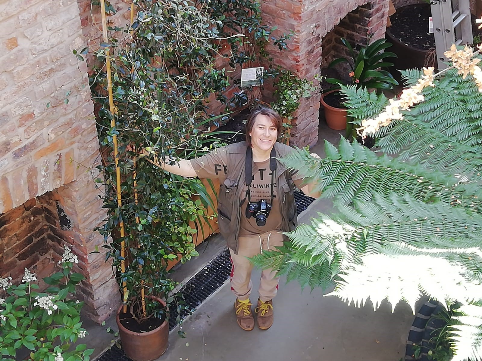 A photograph of Andrea Ku from the above looking down as Andrea is surrounded by garden foliage