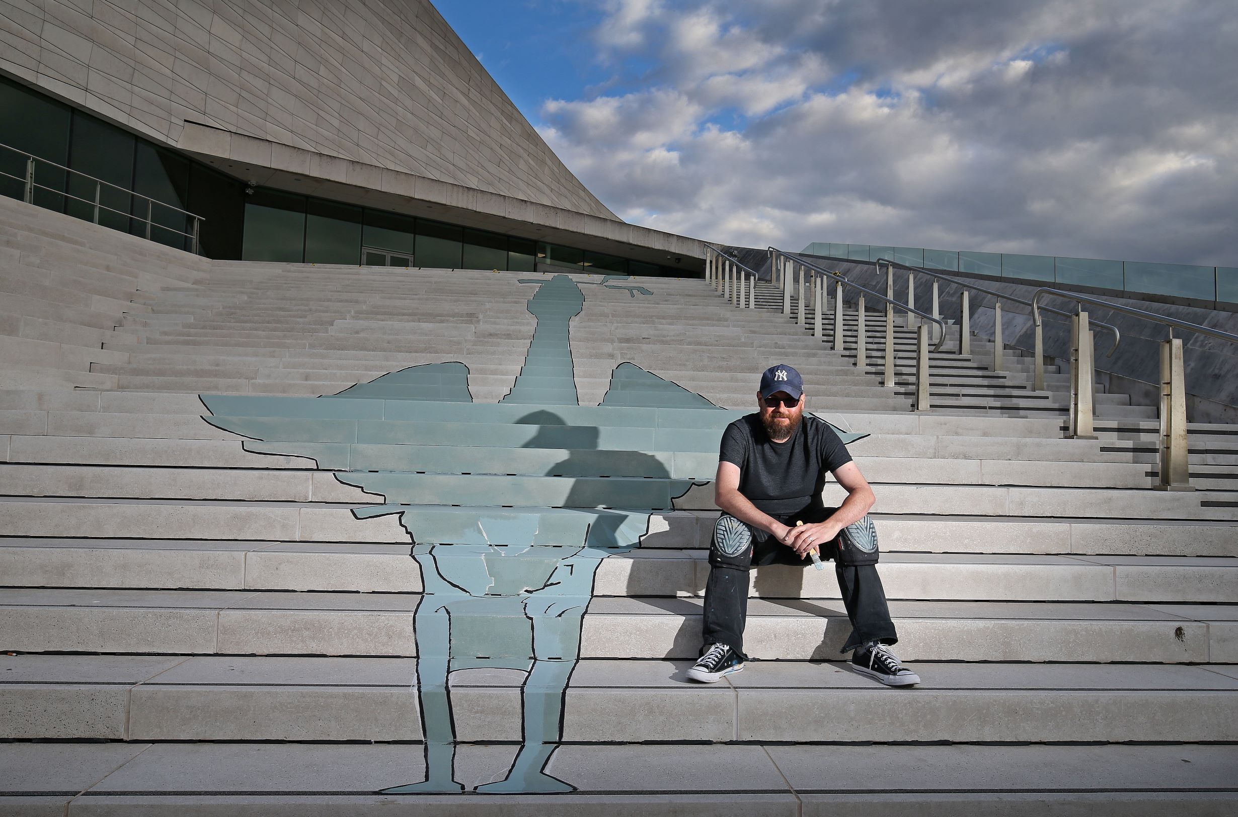 Artist on steps of Liverpool Museum next to a blue liver bird painted across each of the steps to his left