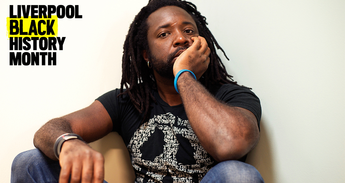 Marlon James in a black t shirt and blue jeans for writing on the wall