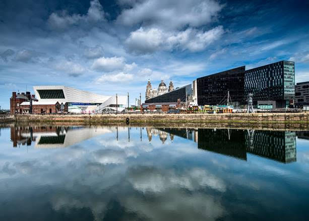 Liverpool docks and museum on the waterfront reflected in the dock against a blue sky with white clouds