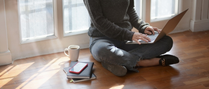adult sitting on floor on laptop with books and a coffee and phone to the side