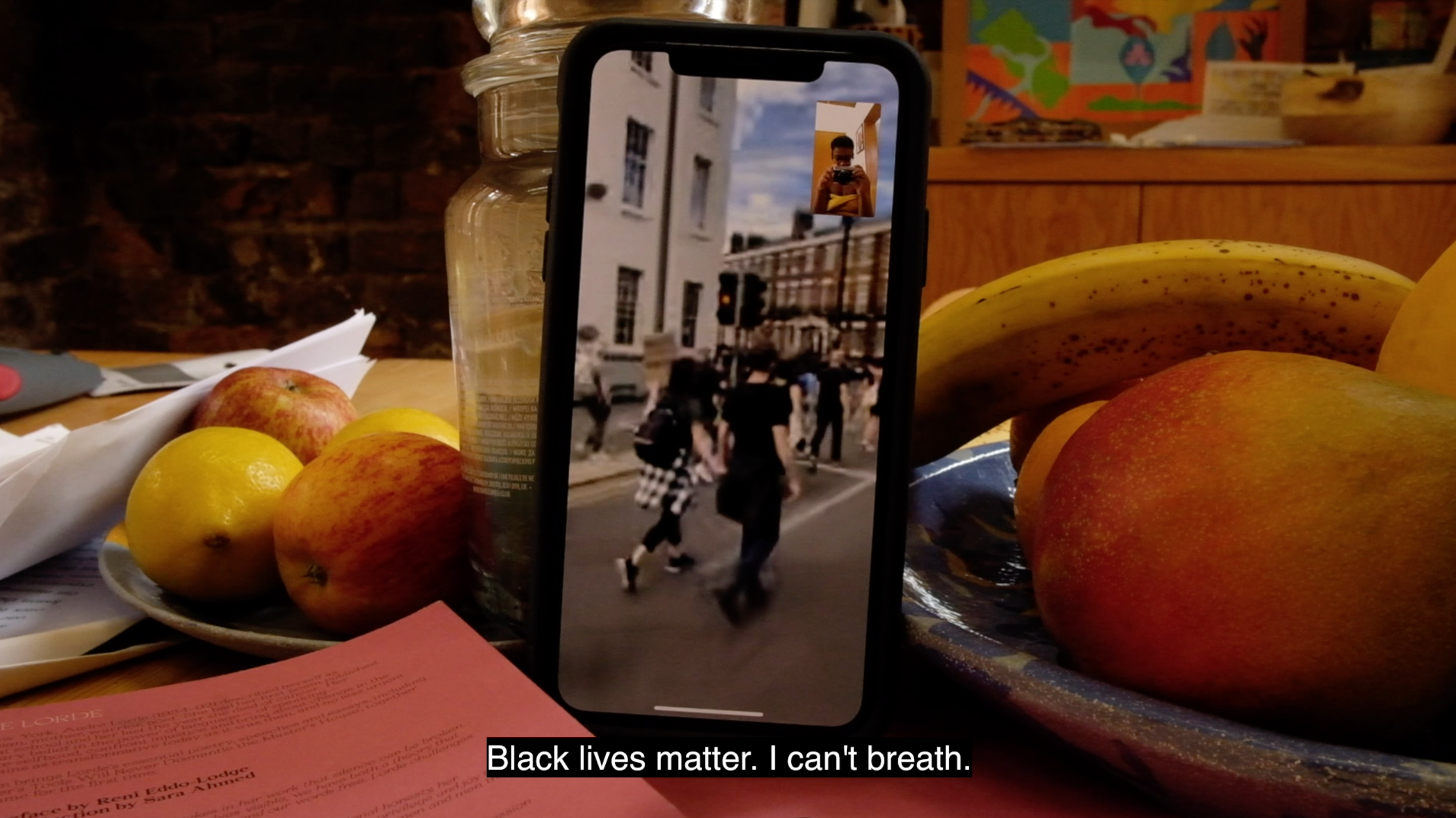phone on a tablet with video showing; on the table is a fruit bowl with fruit in and the rest of the background is blurred - its part of kiara mohamed film