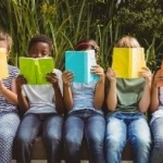 row of children sitting holding books open in front of their faces reading