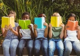 row of children sitting holding books open in front of their faces reading