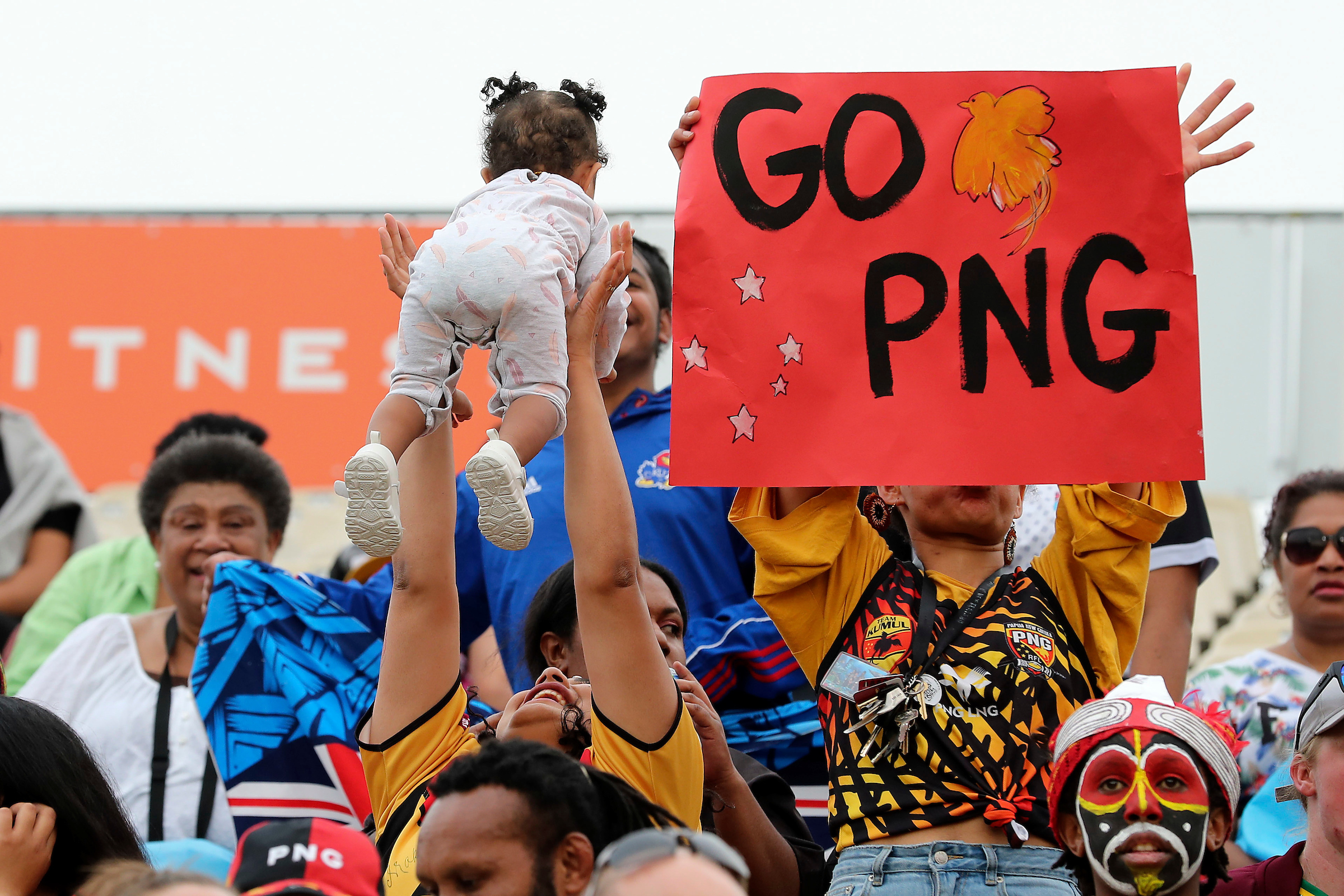rlwc image of people celebrating with a lady throwing a baby in the air and a woman holding a sign saying GO PNG