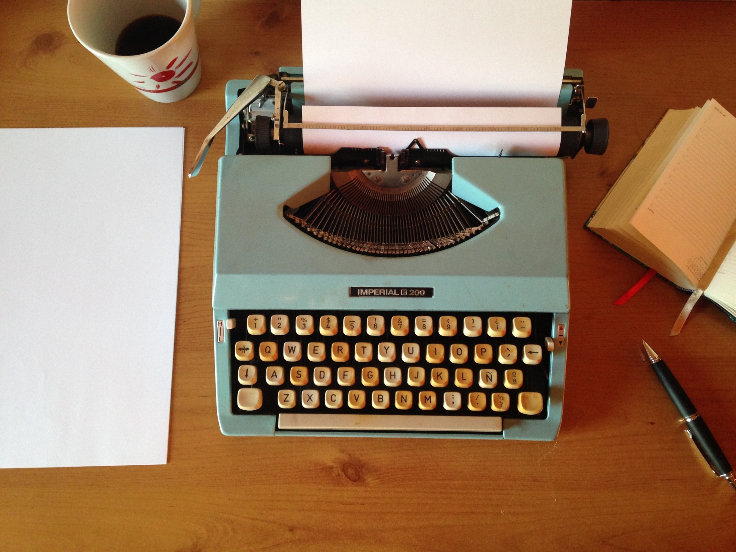 green typewriter on a brown table with white paper next to the left of typewriter