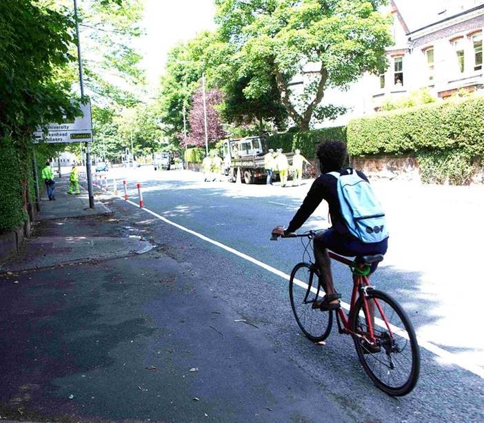 person on bike riding down cycle lane on road surrounded by trees and residential area