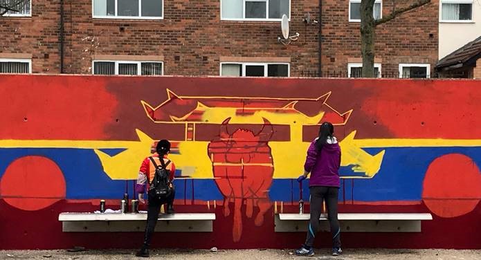 two people painting a mural on a wall in red, yellow and blue