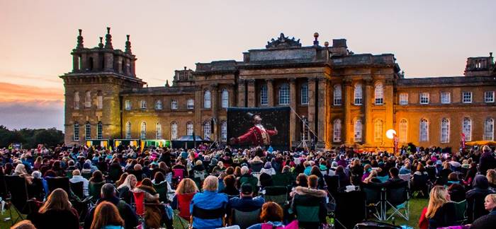 the greatest showman on a outdoor cinea screen at blenheim palace at dusk surrounded by crowds