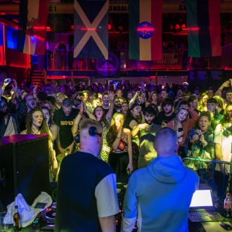 view of a nightclub scene from behind two djs