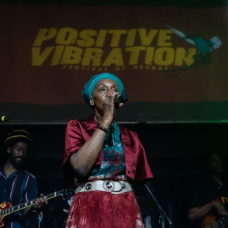 person stoof on stage with mircophone in front of sign that says positive vibration