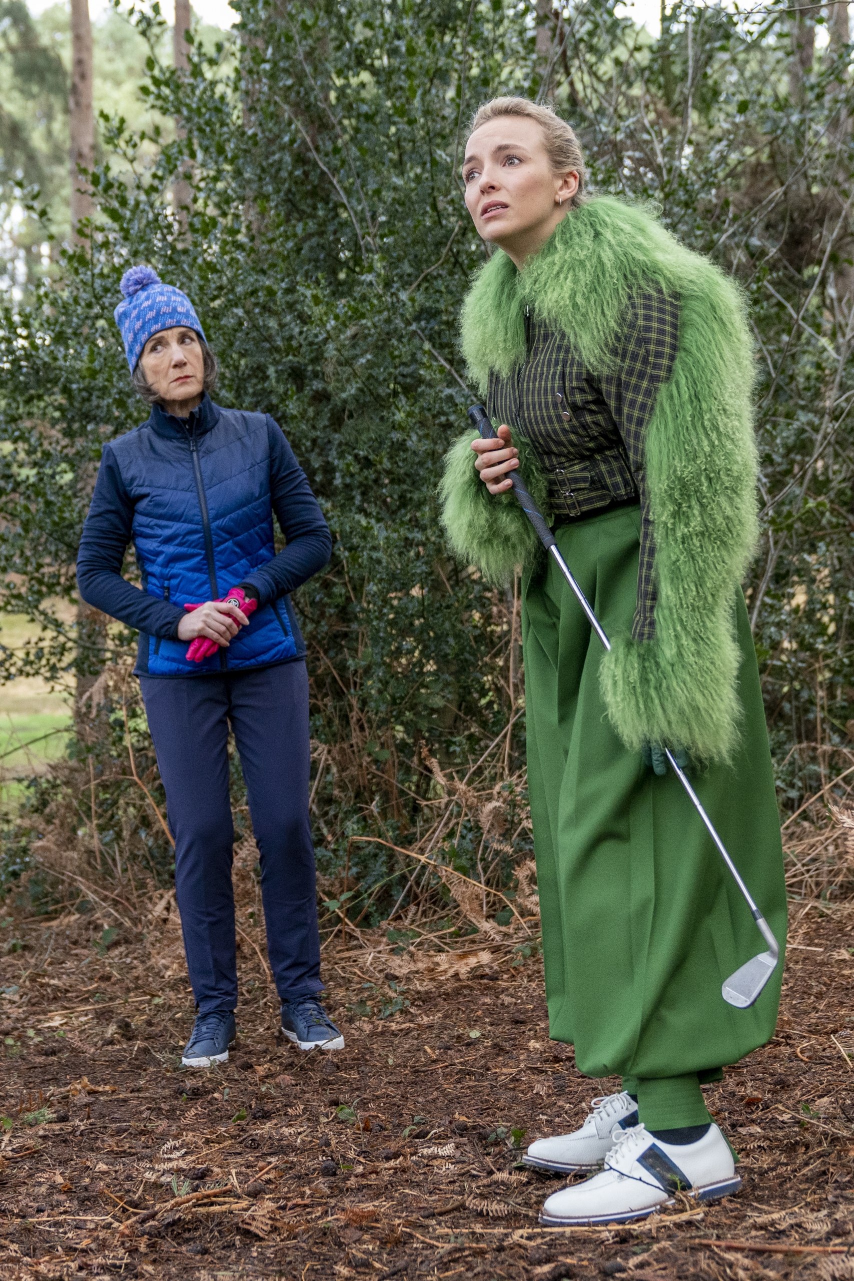lady in green coat holding a golf stick in a forest next to a lady in a blue jacket and jeans a blue hat for national museums liverpool