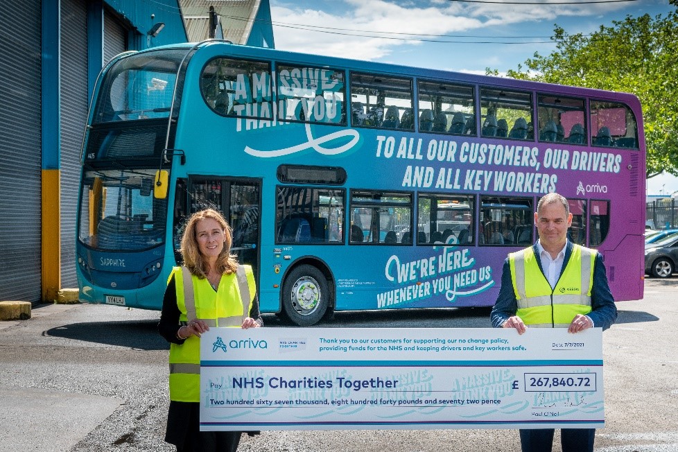 man and woman holding a giant checque in front of an arriva bus
