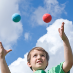 child juggling balls against a blue sky