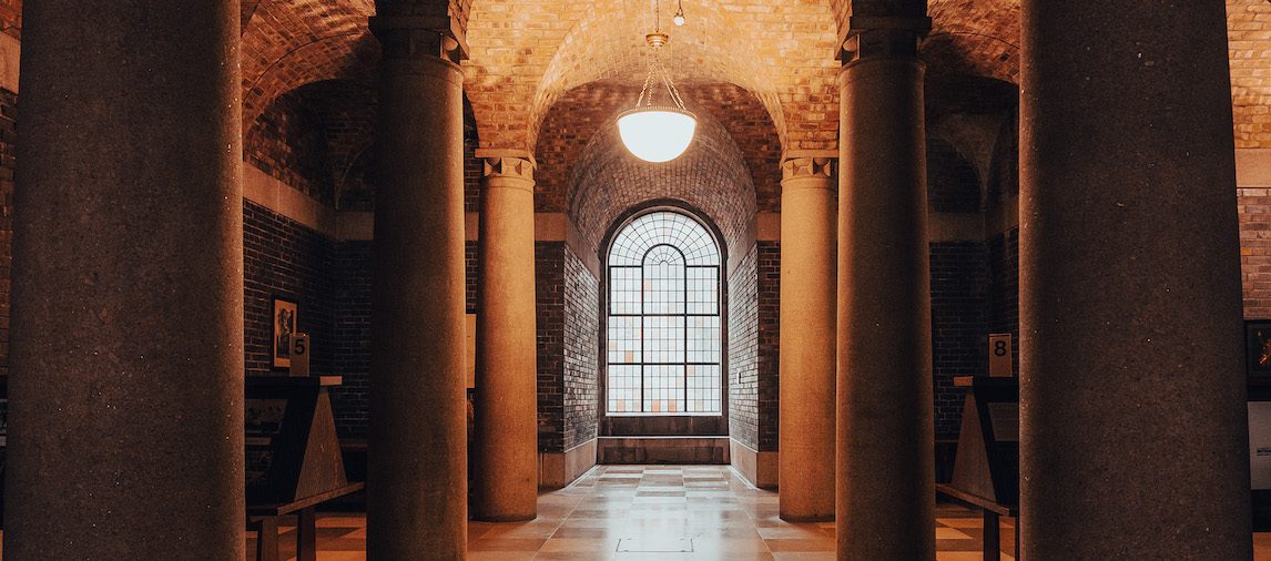 lutyens crypt under the liverypool metropolitan cathedral, marble floor and four pillars flank the sides of the imager with a clear window at the back and a curved lamp hanging from the ceiling