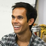 Sub Das smiling at someone off camera, wearing black and white check shirt and black, yellow and silver lanterns in background