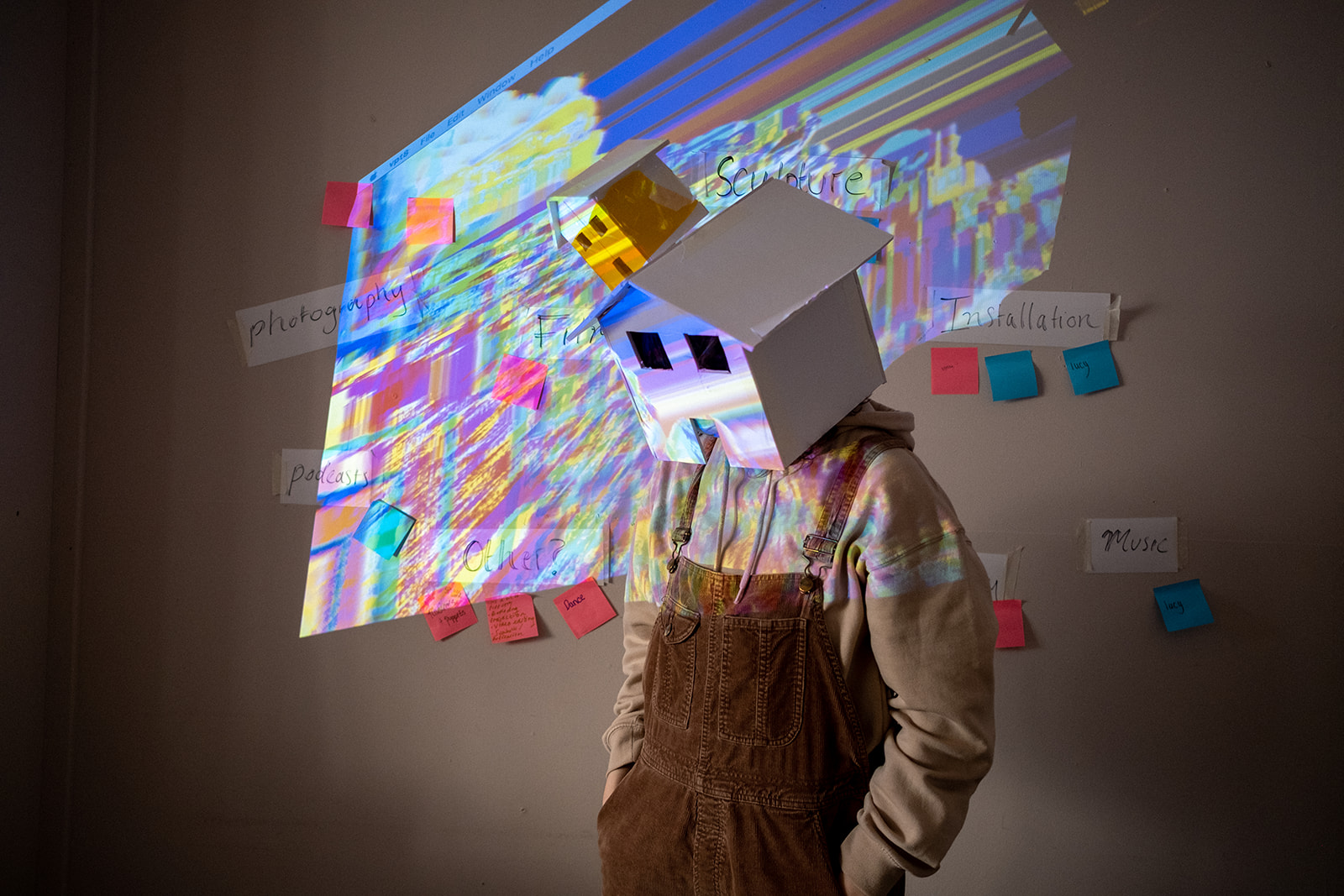 individual with a house shaped cut out box on their head with pictures projected on the wall behind them as part of art project