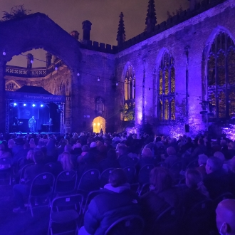 liverpool theatre festival at night in grounds of bombed out church, lighting is blue, view from behind audience looking at a stage