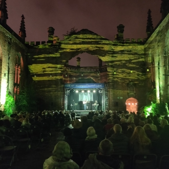 liverpool theatre festival at night in grounds of bombed out church, lighting is green, view from behind audience looking at a stage