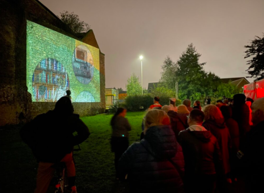 people at night watching a film projected on to the side of everton library