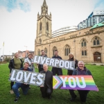 men and women standing outside church holding colourful signs that say liverpool loves you