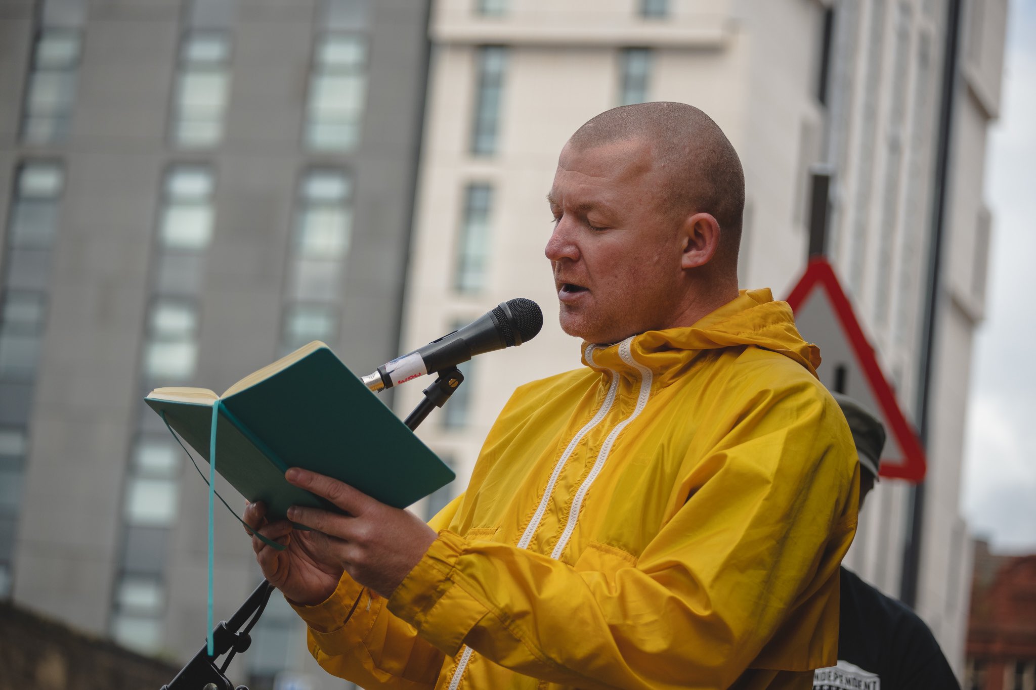 writers bloc writer roy in yellow jacket reading from a green noebook for writing on the wall