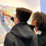 two students of mixed race pointing at a map on a wall for colonial legacies project