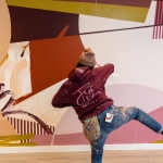 person in red jumper and jeans painting a mural on a wall