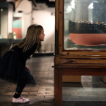 little girl bending down to look at a ship in a museum cabinet at national museums liverpool