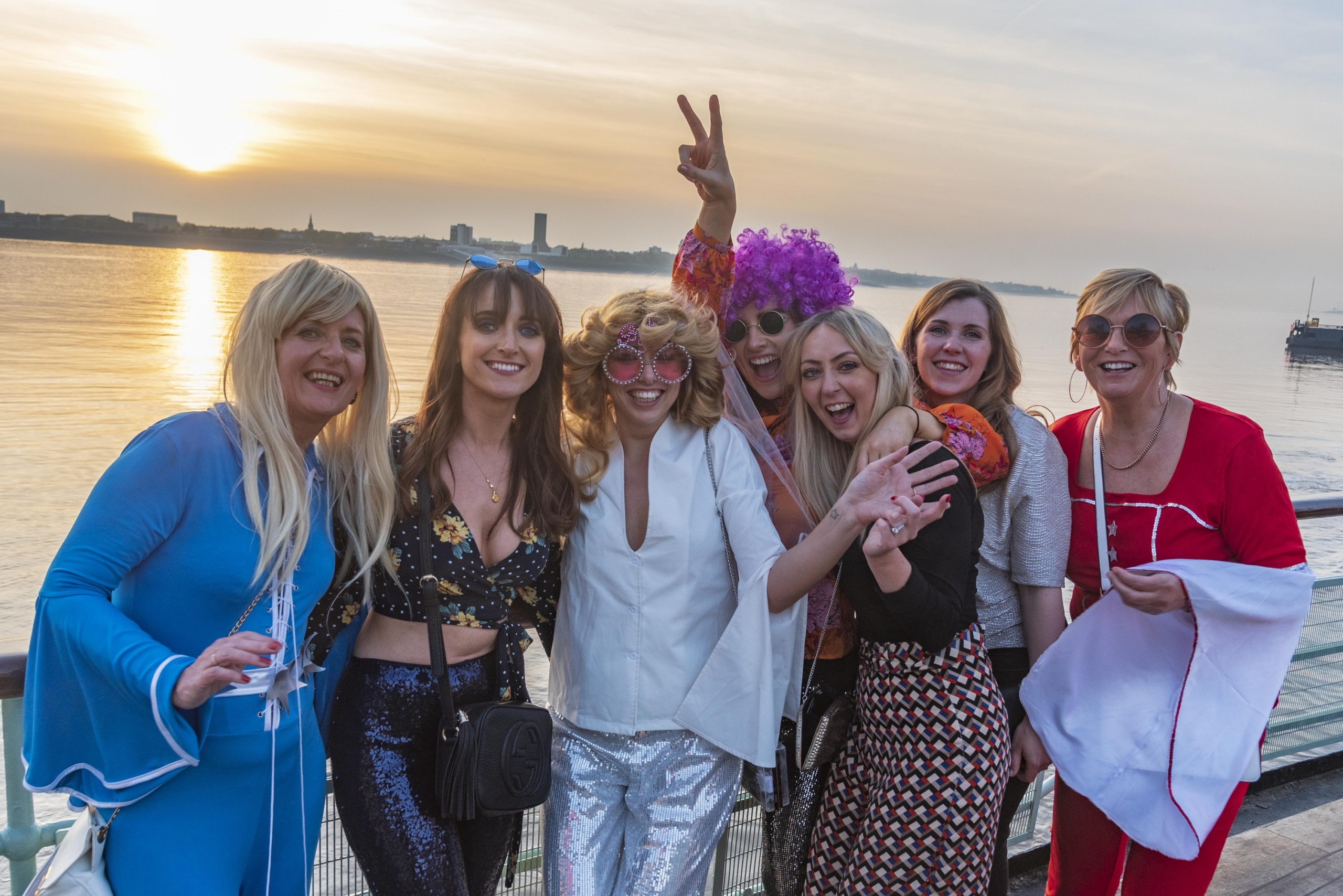 mersey ferries evening cruise featuring ladies in abba costume against a sunset