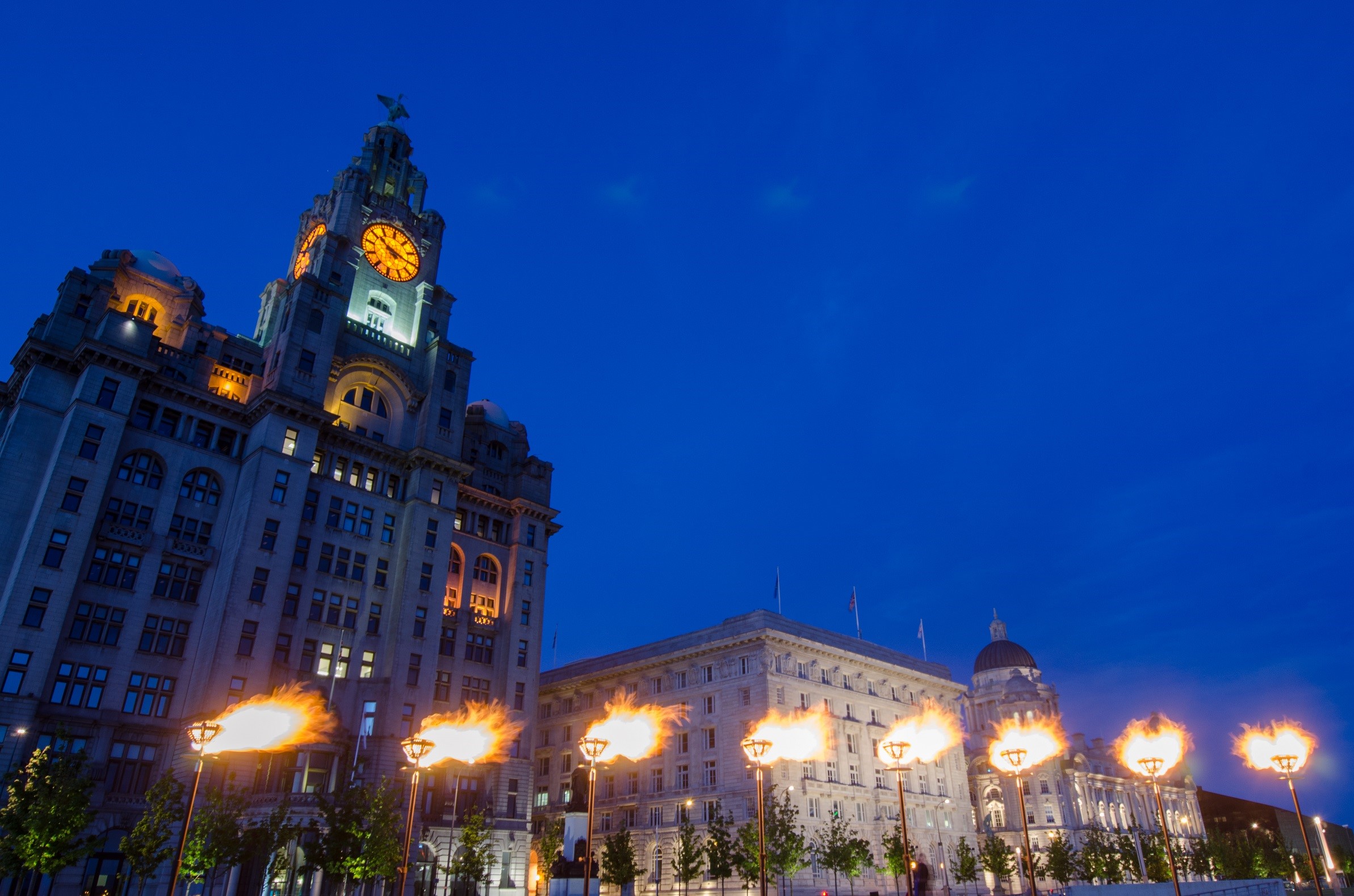 royal lliver building alongside cunard building at night with seven light up flames in front