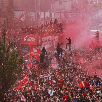crowds surround an open top bus in 2019 with red flares for LFC Parade