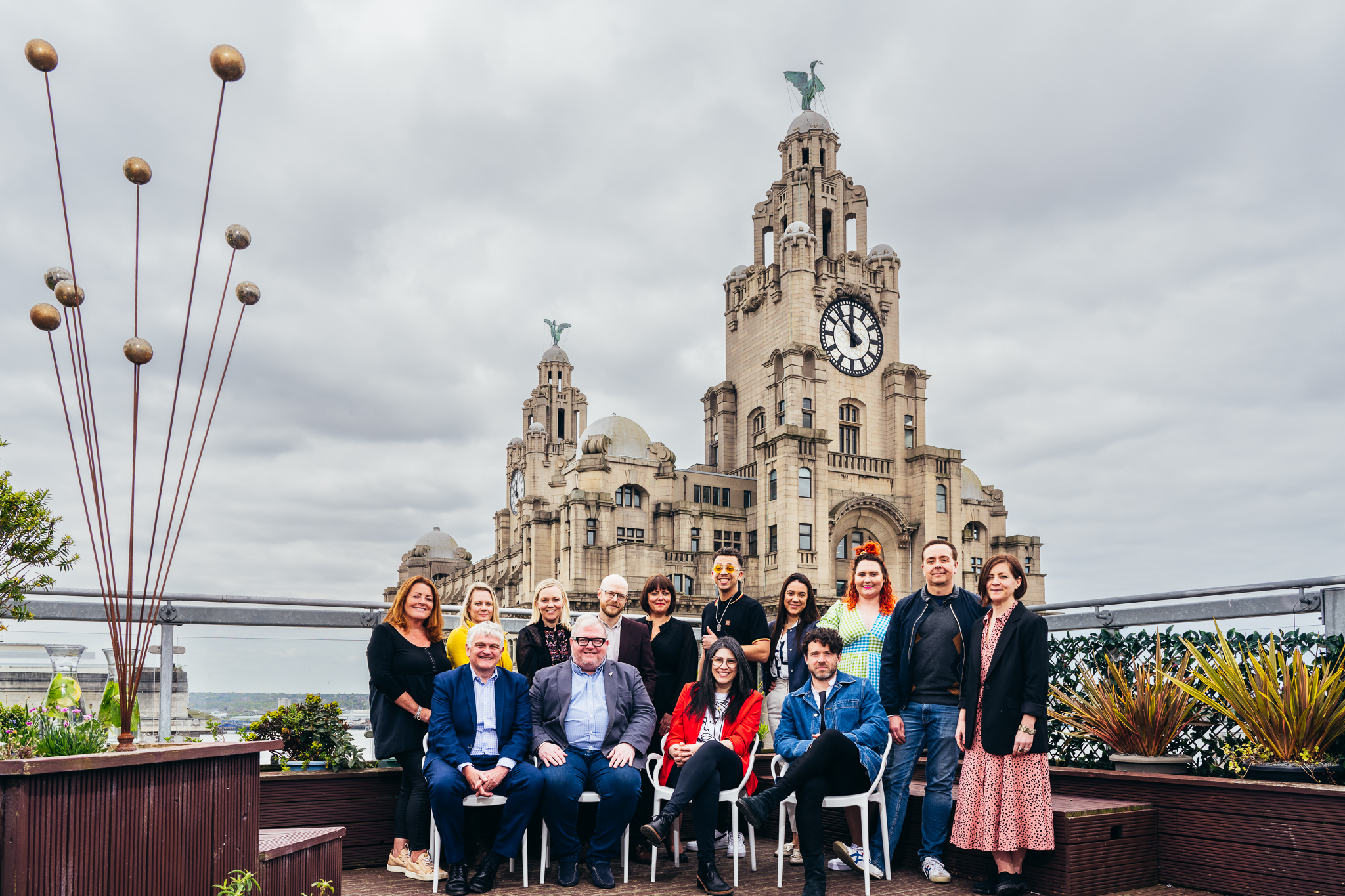 men and women sat on the rooftop of oh me oh my in front of royal liver building in background