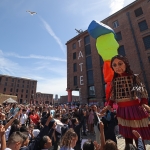 little amal a giant walking wooden puppet in front of tate liverpool in the albert dock surrounded by crowds
