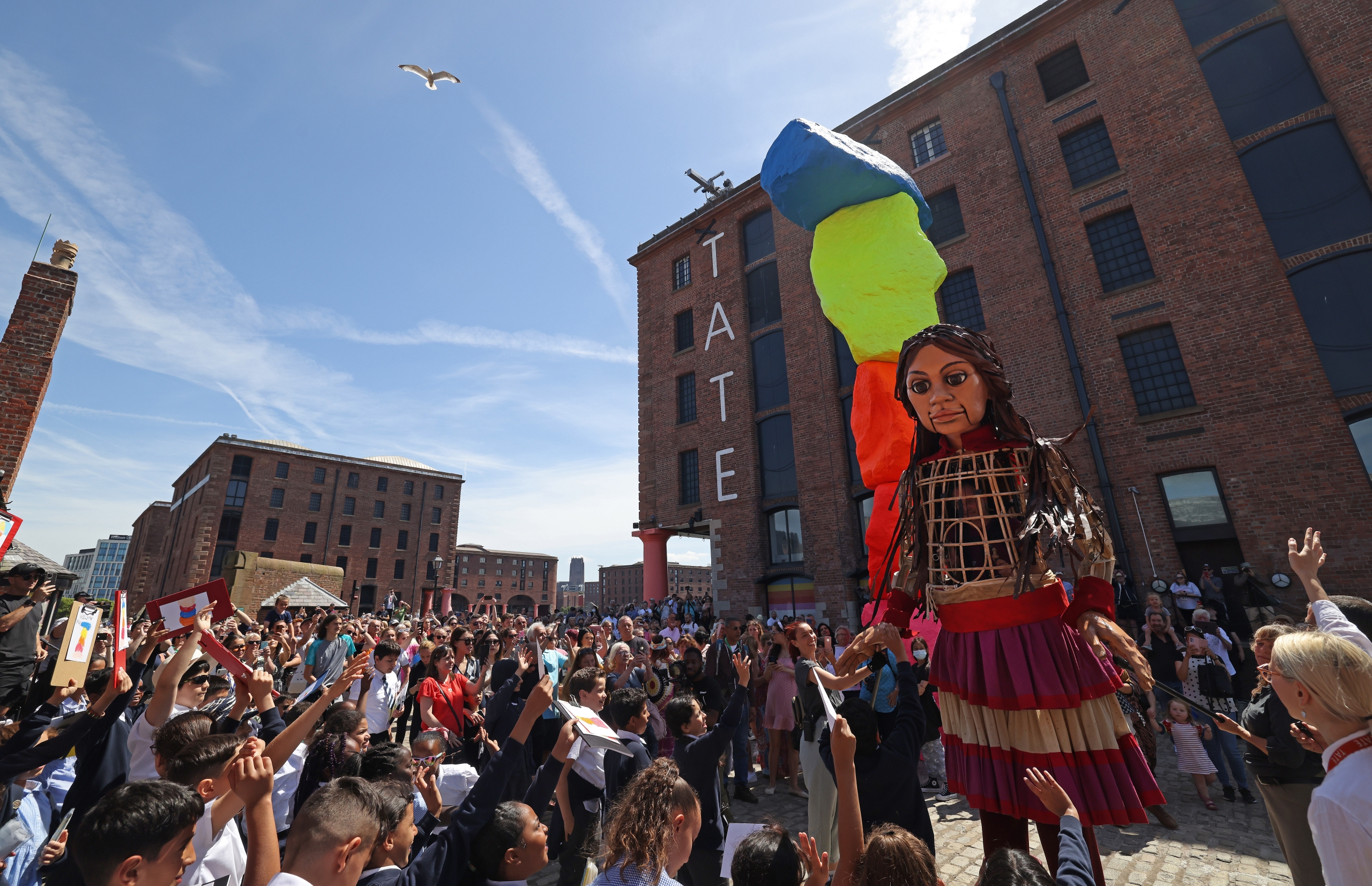 little amal a giant walking wooden puppet in front of tate liverpool in the albert dock surrounded by crowds