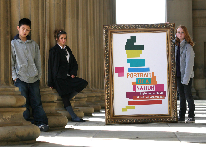 three young teenagers standing near a frame with an image of portrait of a nation in front of St George's Hall