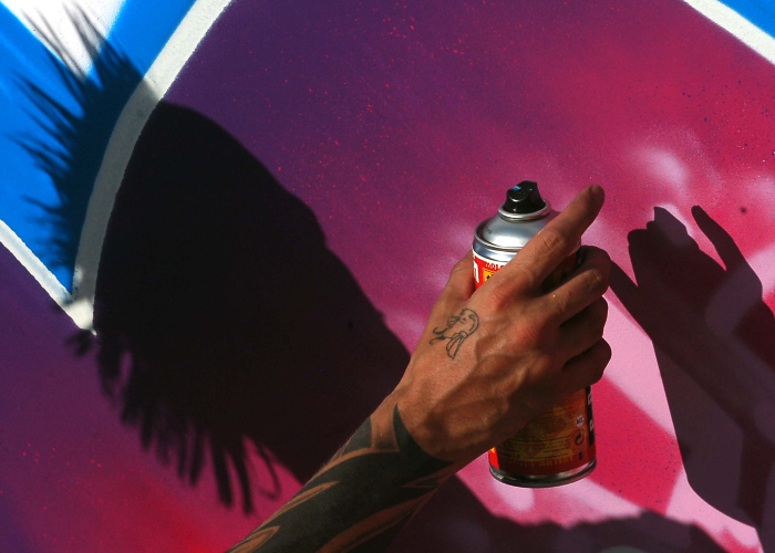 hand with a tattoo holding a spray can creating graffiti art