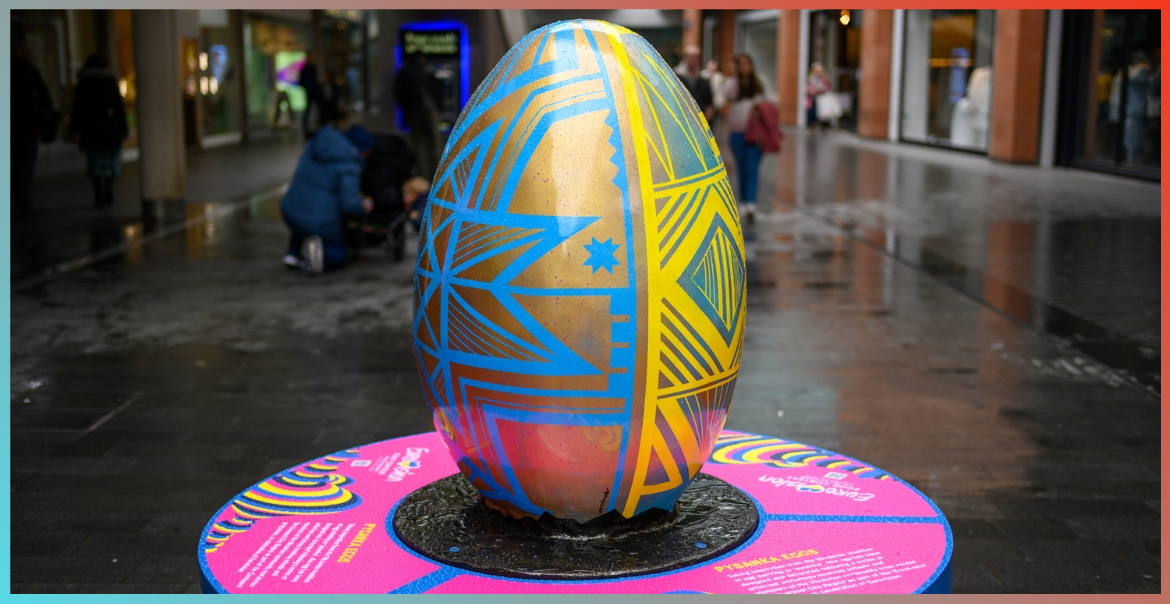 A large egg sculpture painted gold with geometric patterns in blue and yellow located in Liverpool One high street,