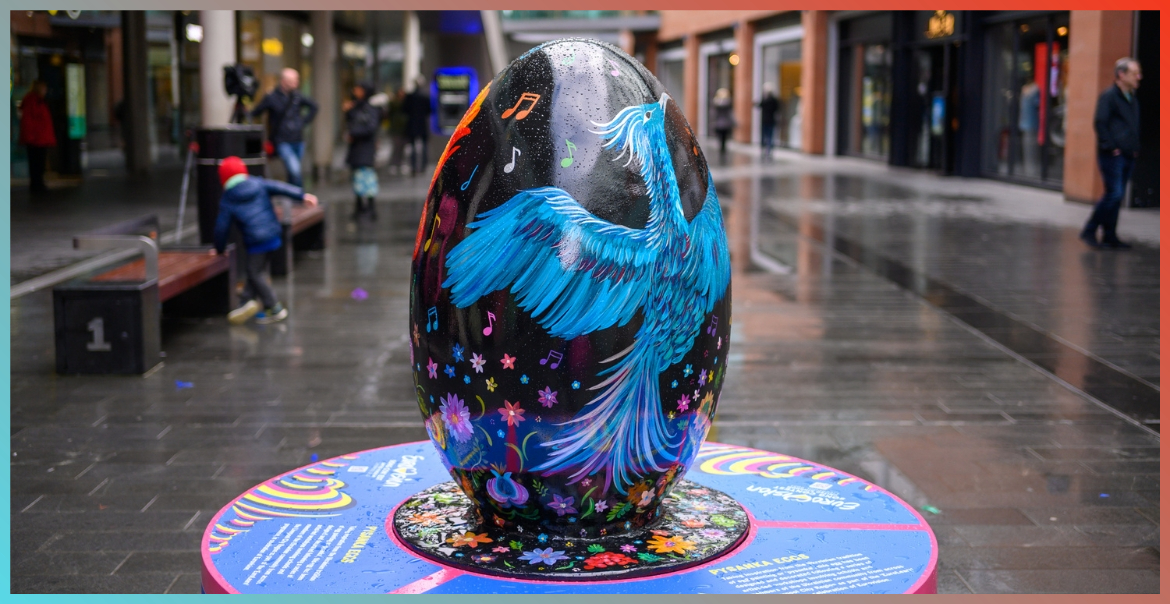 A large egg sculpture painted black with a large blue bird on display in Liverpool One high street.