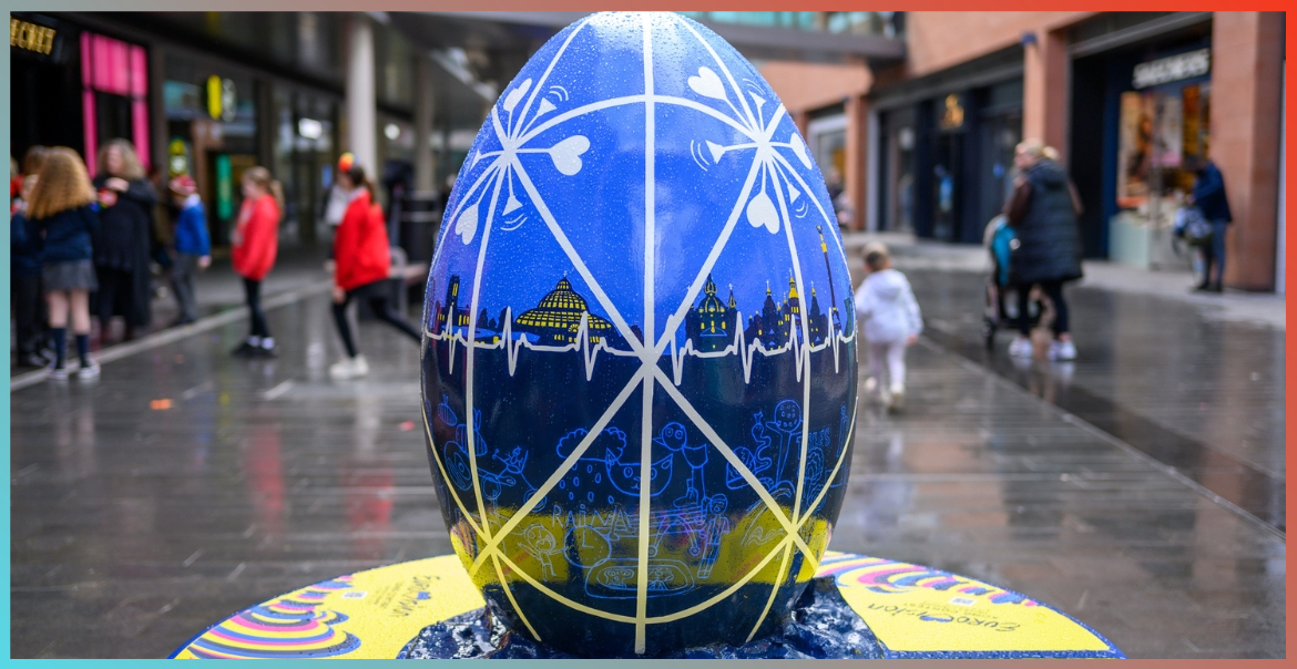 A large egg sculpture painted with the Liverpool waterfront in blue colours. A white lined pattern covers the top. The egg sculpture is in Liverpool One high street.
