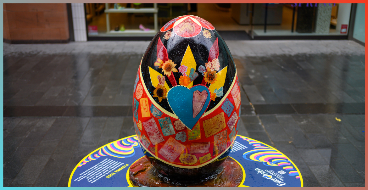 A large egg sculpture painted black with yellow triangular shapes with a blue heart and sunflowers. This is displayed in Liverpool One high street as part of an art installation.