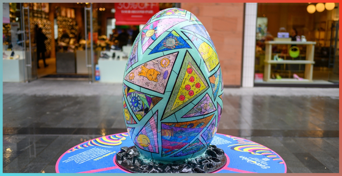 A large egg sculpture panted a teal colour with triangular shapes. Within each triangular shape is a unique painting. This sculpture is in Liverpool One high street.