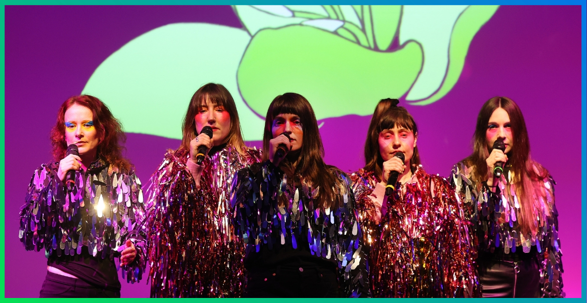 A photograph of Natalie McCool with Stealing Sheep singing on stage with glittery jackets on.