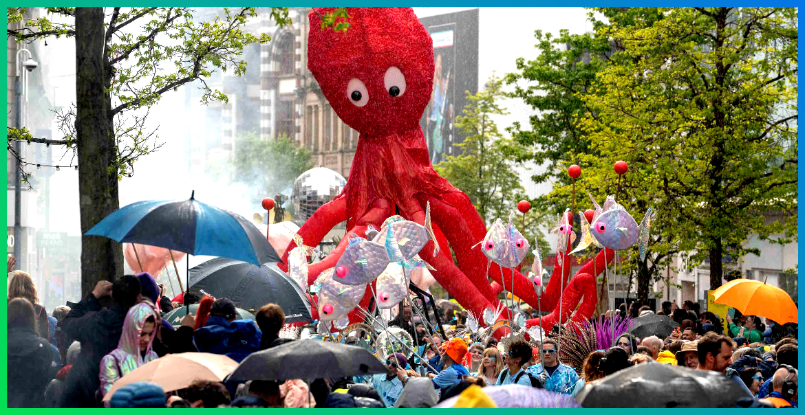 Red octopus puppet walking the streets of Liverpool in front of crowds of people