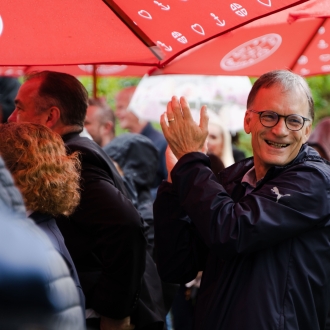 A man clapping in a crowd of people outside on a rainy day.