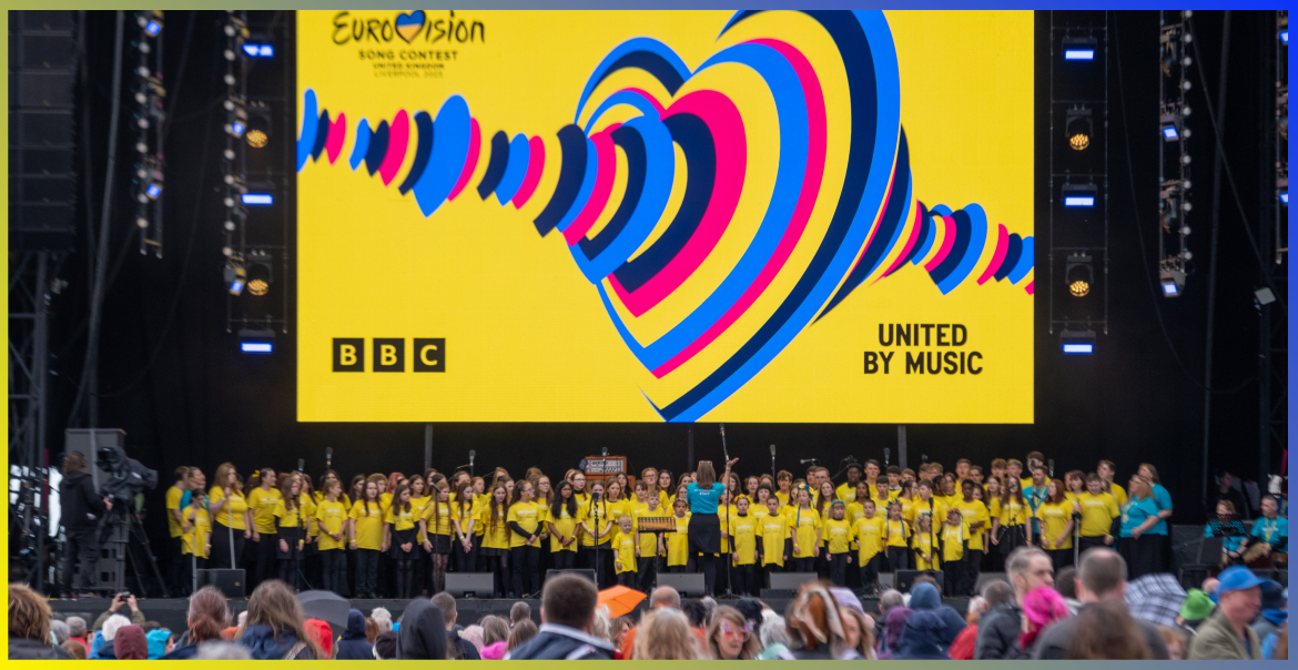 A large children's choir performing on the Eurovision Village stage.